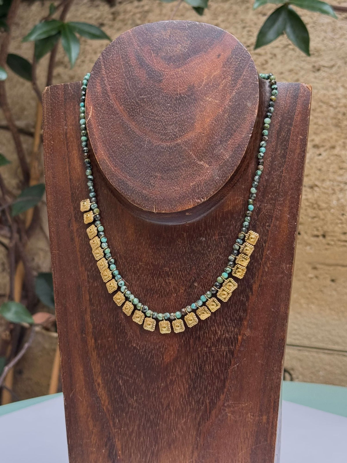 Collier en pierre naturelle verte et médailles carrées dorées sur buste en bois