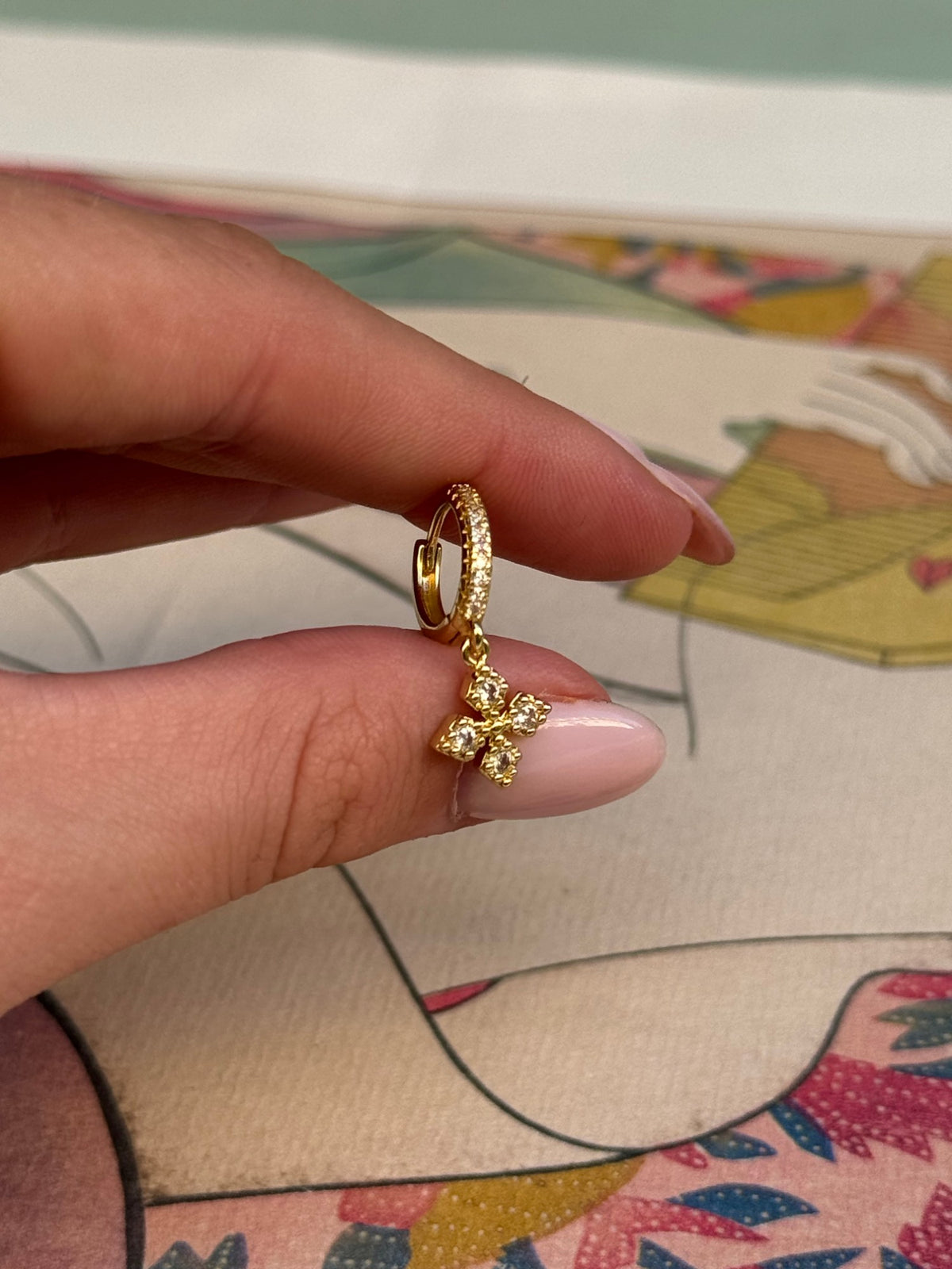 Détail d'une petite créole dorée à strass et de son pendentif fleur