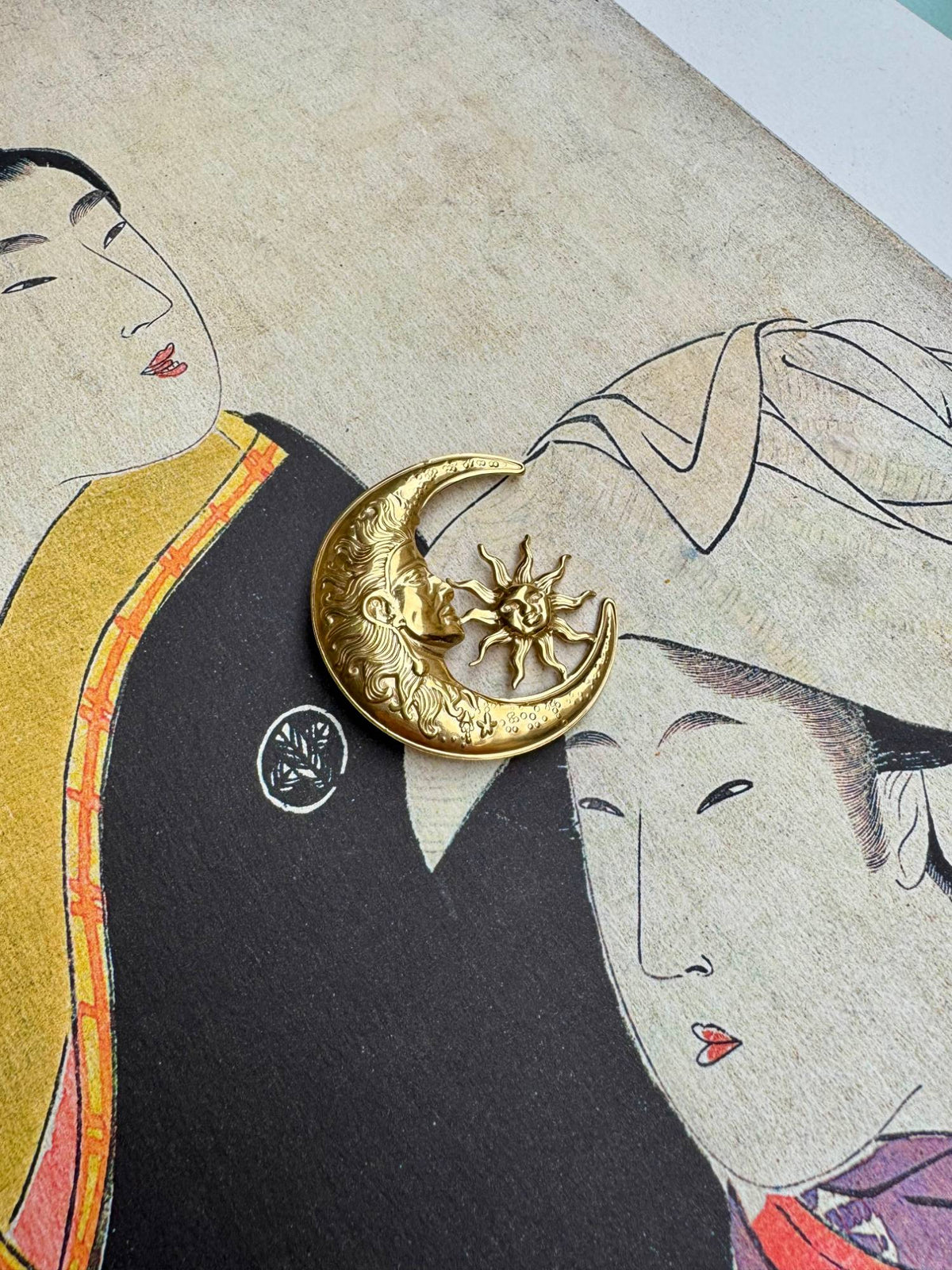 Broche lune et soleil dorée en acier inoxydable posée sur une estampe japonaise