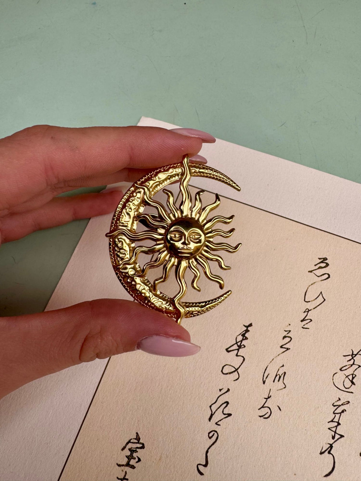 Broche soleil dorée tenue en main, détail du visage du soleil et de ses rayons ondulés