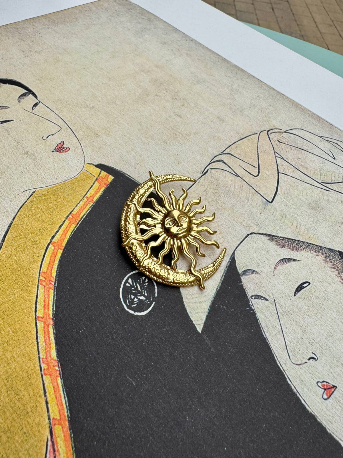 Broche soleil et croissant de lune dorée posée sur une estampe japonaise