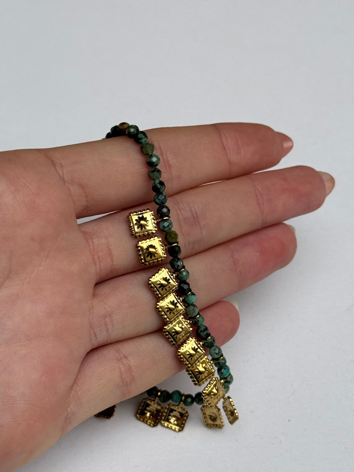 Collier bohème en pierre naturelle verte et médailles dorées tenu en main