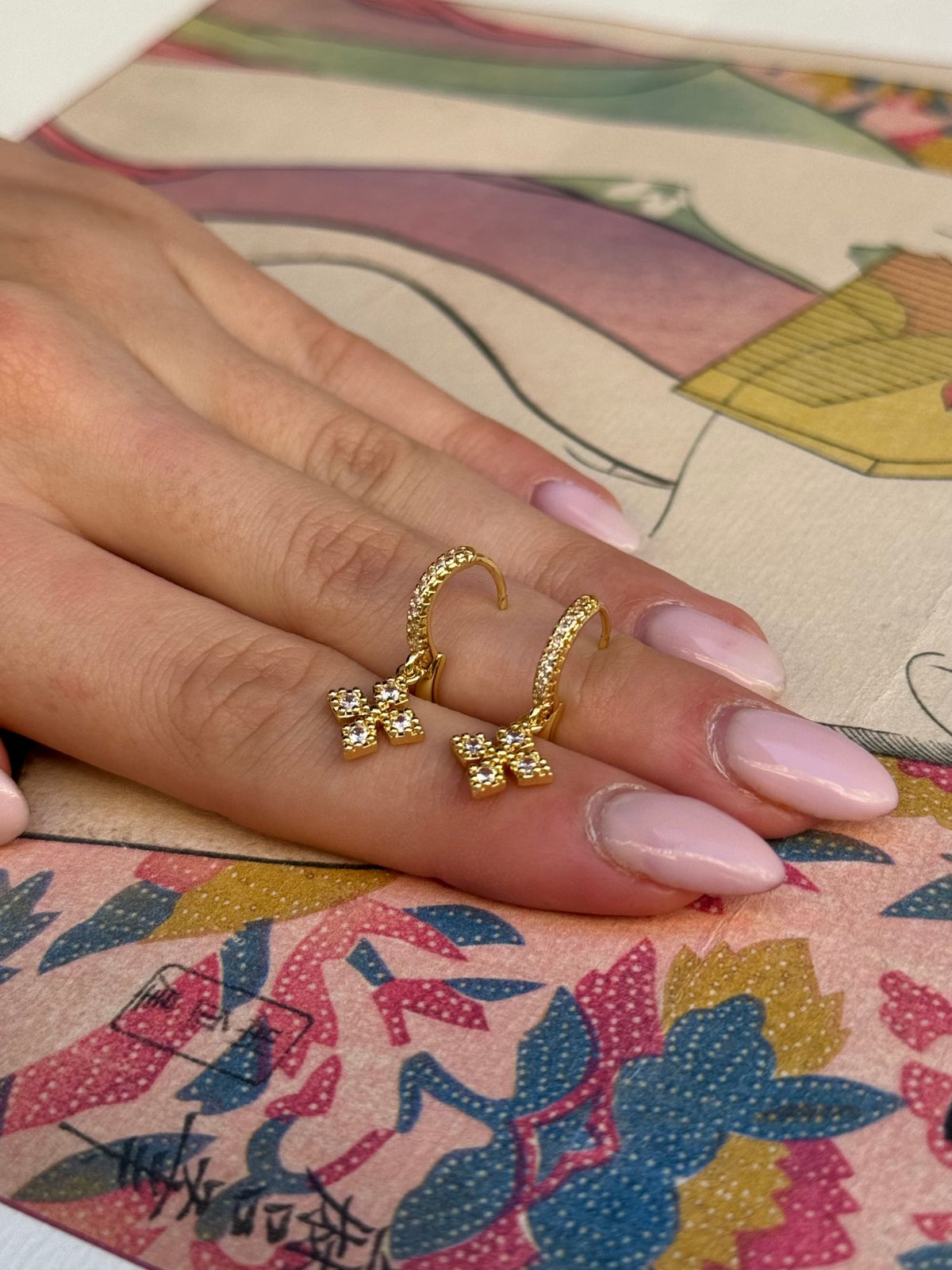 Créoles dorées à fermoir clip avec fleur en strass, portées sur la main