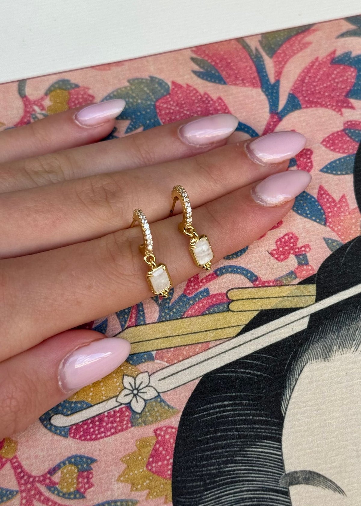 Paire de mini créoles dorées serties de strass blancs et pierre blanche, portées sur la main