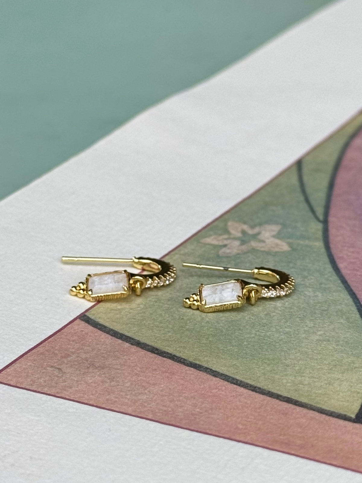 Détail des petites créoles dorées à strass et de leur pendentif pierre blanche